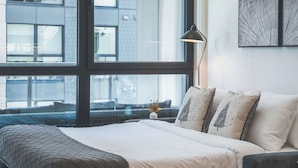 Une chambre à coucher moderne avec une grande fenêtre, un lit recouvert d’une couvre-lit à motifs et une lampe de chevet.