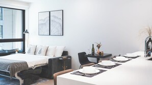 Une chambre moderne avec un lit, une table à manger dressée pour quatre personnes, une petite table d’appoint et une grande fenêtre.