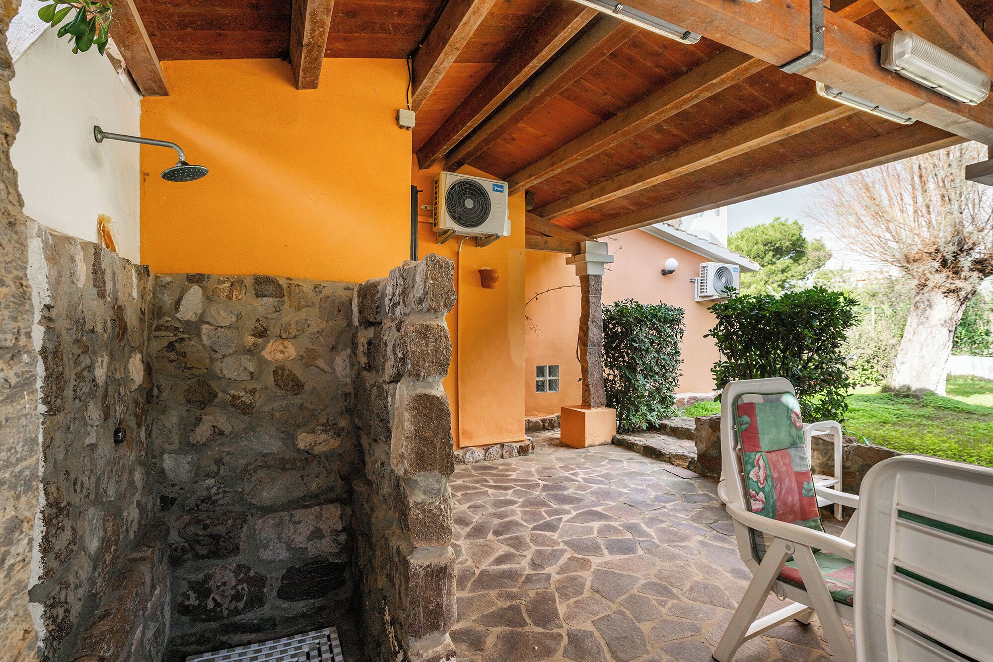 Une cheminée en pierre, un espace extérieur aménagé avec un fauteuil, et une terrasse couverte avec un plafond en bois.