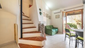 Un escalier dont la base est en pierre mène à un espace de vie comprenant un canapé vert, une table à manger et des chaises.