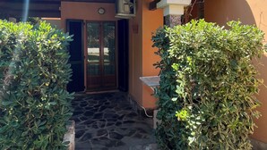 Un bâtiment avec un toit en tuiles, une entrée en pierre et une petite table sur laquelle est posé un pot de fleurs.