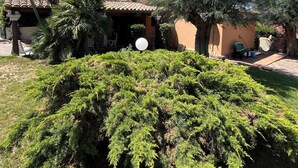 Une maison avec un toit en tuiles, entourée de différents arbres et d’une pelouse bien entretenue.