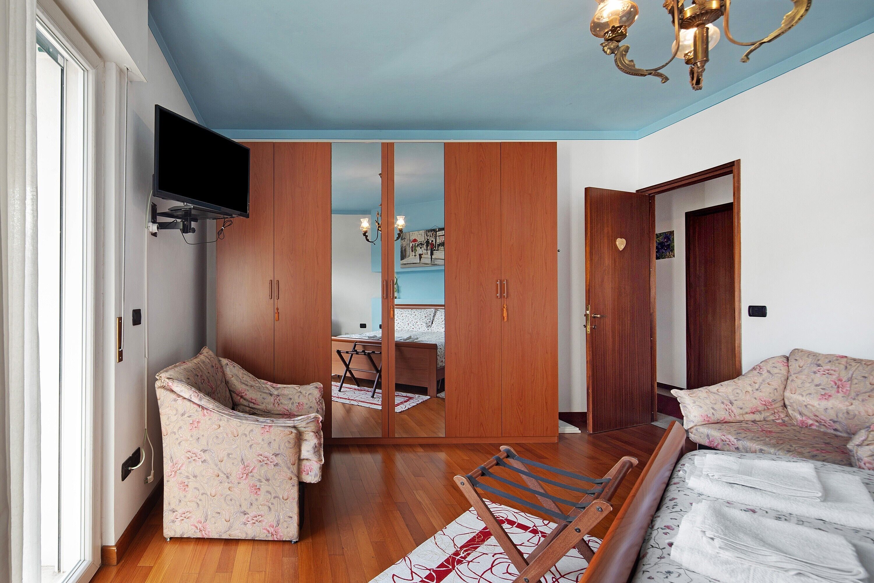 Ein Schlafzimmer mit Bett, Sessel, Fernseher, Kleiderschrank und Spiegel.