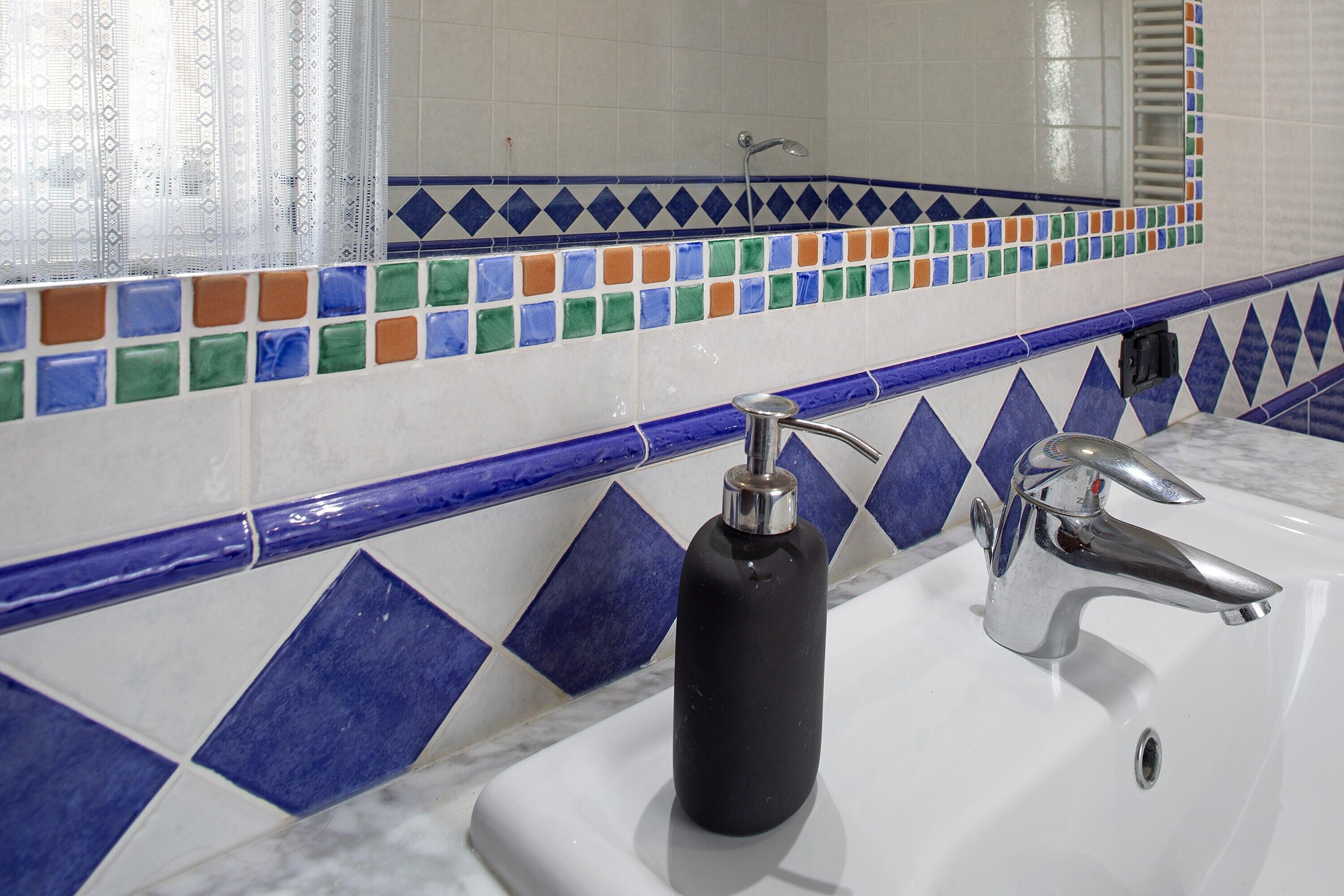 Une salle de bain avec un lavabo blanc, un distributeur de savon noir et un robinet chromé.