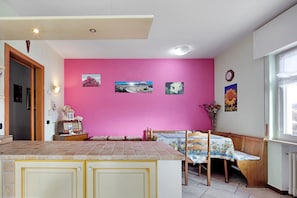 Une cuisine avec un mur rose, des meubles en bois, un plan de travail carrelé et un coin repas avec une table et des chaises.