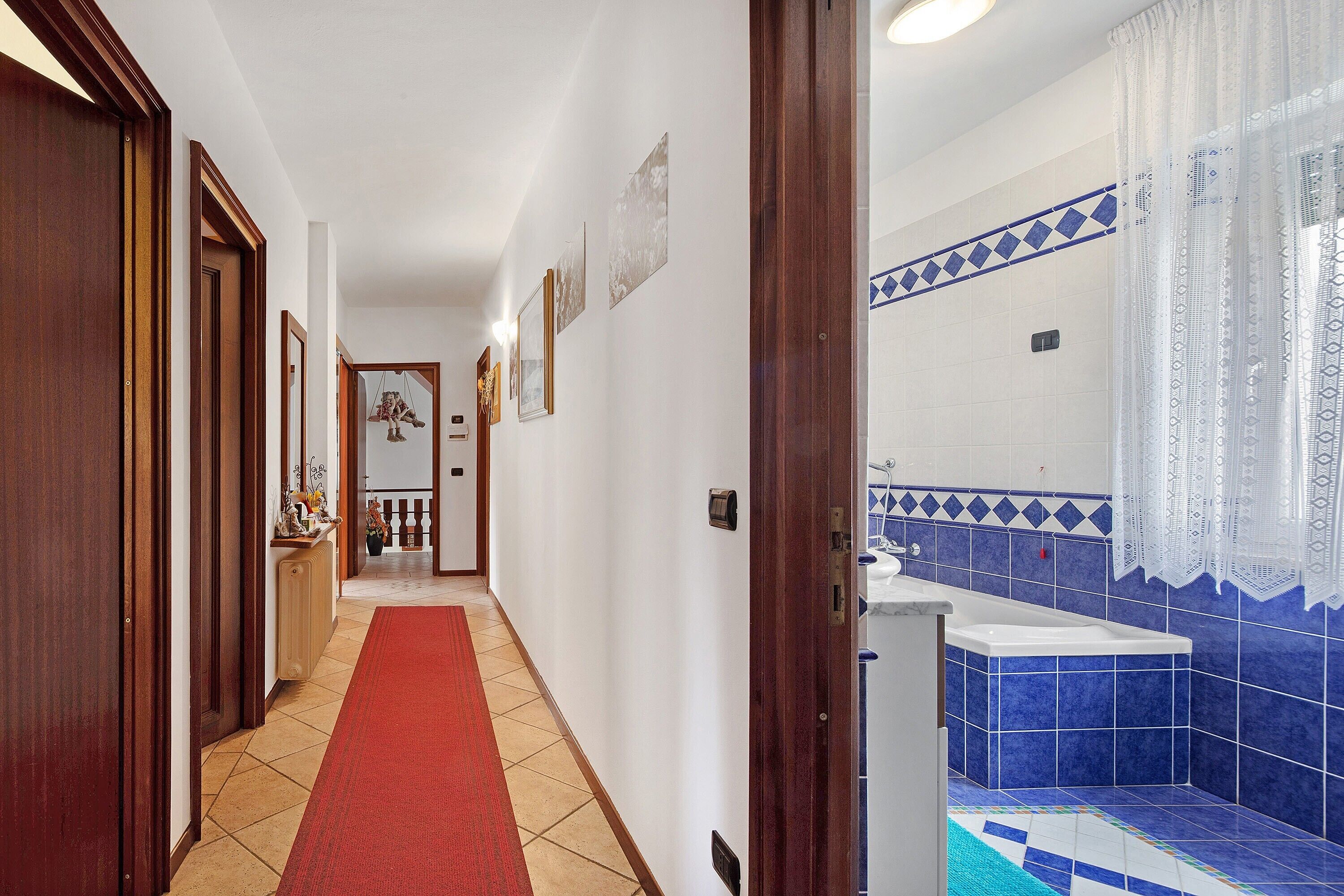Un pasillo de hotel con alfombra roja, puertas de madera y un baño con azulejos azules y un lavamanos blanco.
