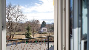 Blick von einem Balkon mit Metallgeländer, blauem Himmel und einem Gebäude in der Ferne.