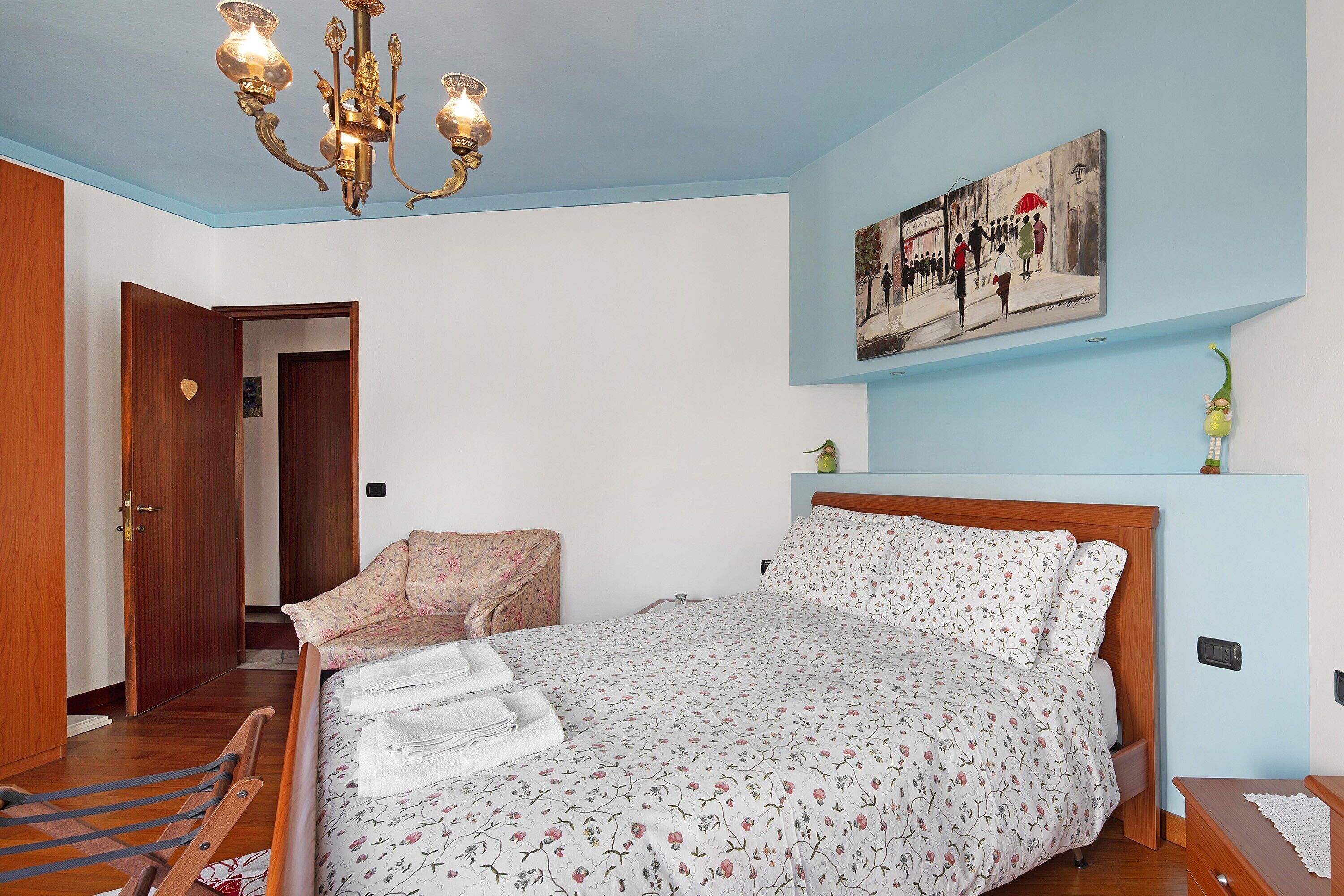 Una camera da letto con un letto, un lampadario, un quadro e una porta in legno.