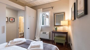 Una camera d'albergo con un letto, una scrivania, una sedia, una lampada e una finestra con tende.