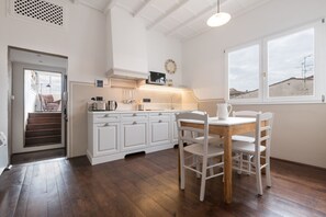 A kitchen with white cabinets, a wooden dining table, and a view through a window. - Santa Maria Novella Skylight Apartment (FIRENZE)
