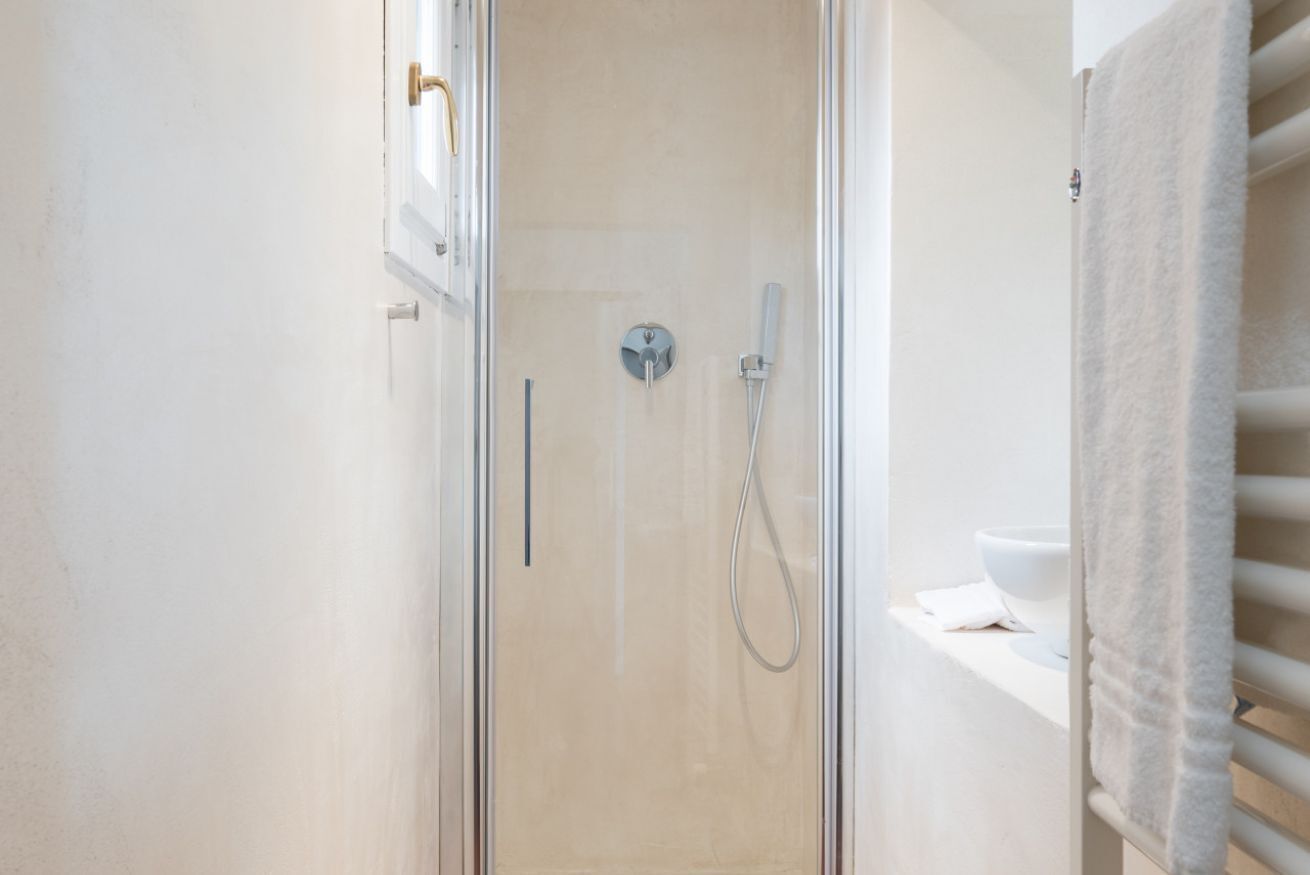 A glass-enclosed shower with a handheld showerhead and a wall-mounted faucet.