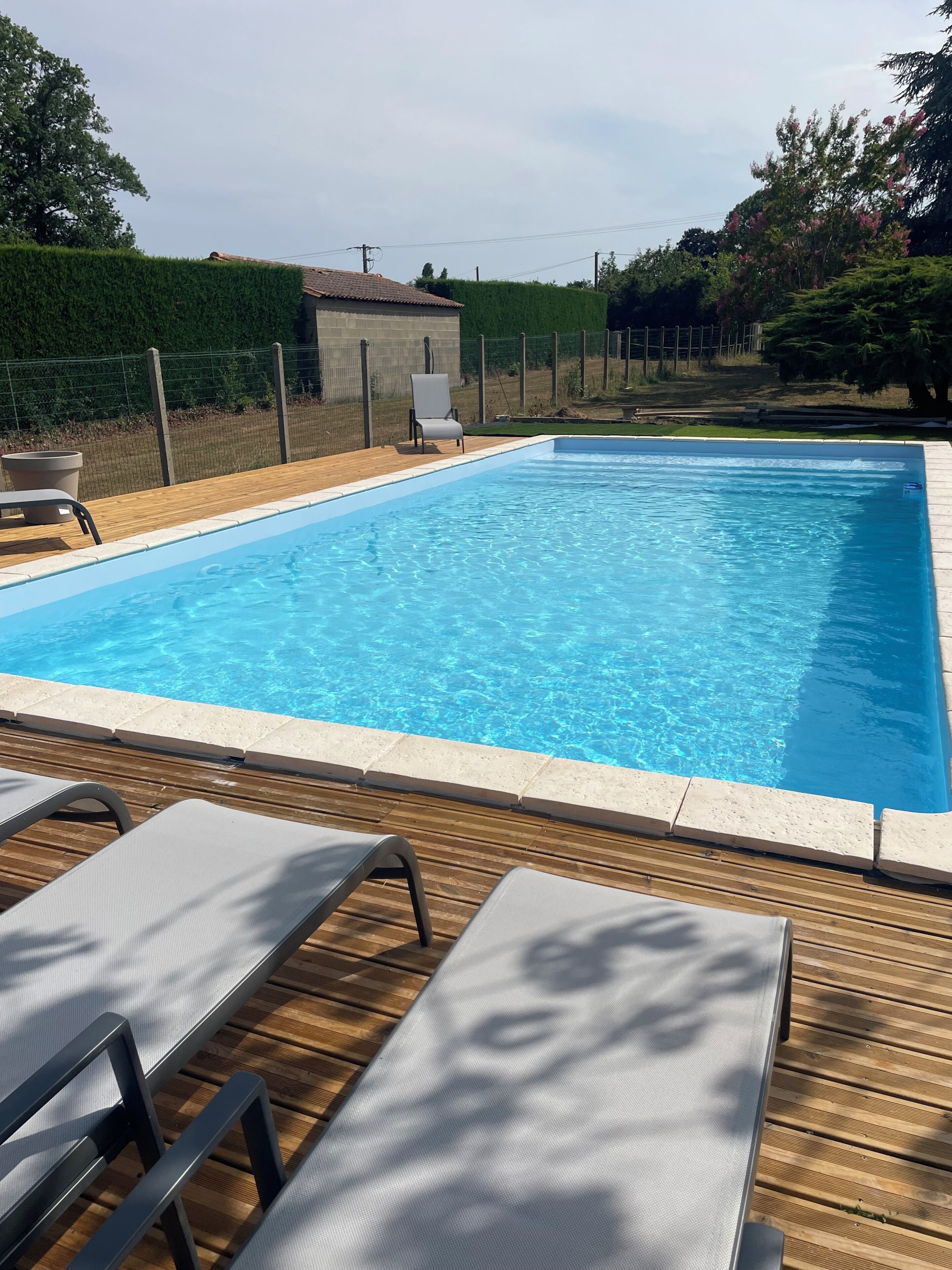 A rectangular swimming pool with a wooden deck and lounge chairs.