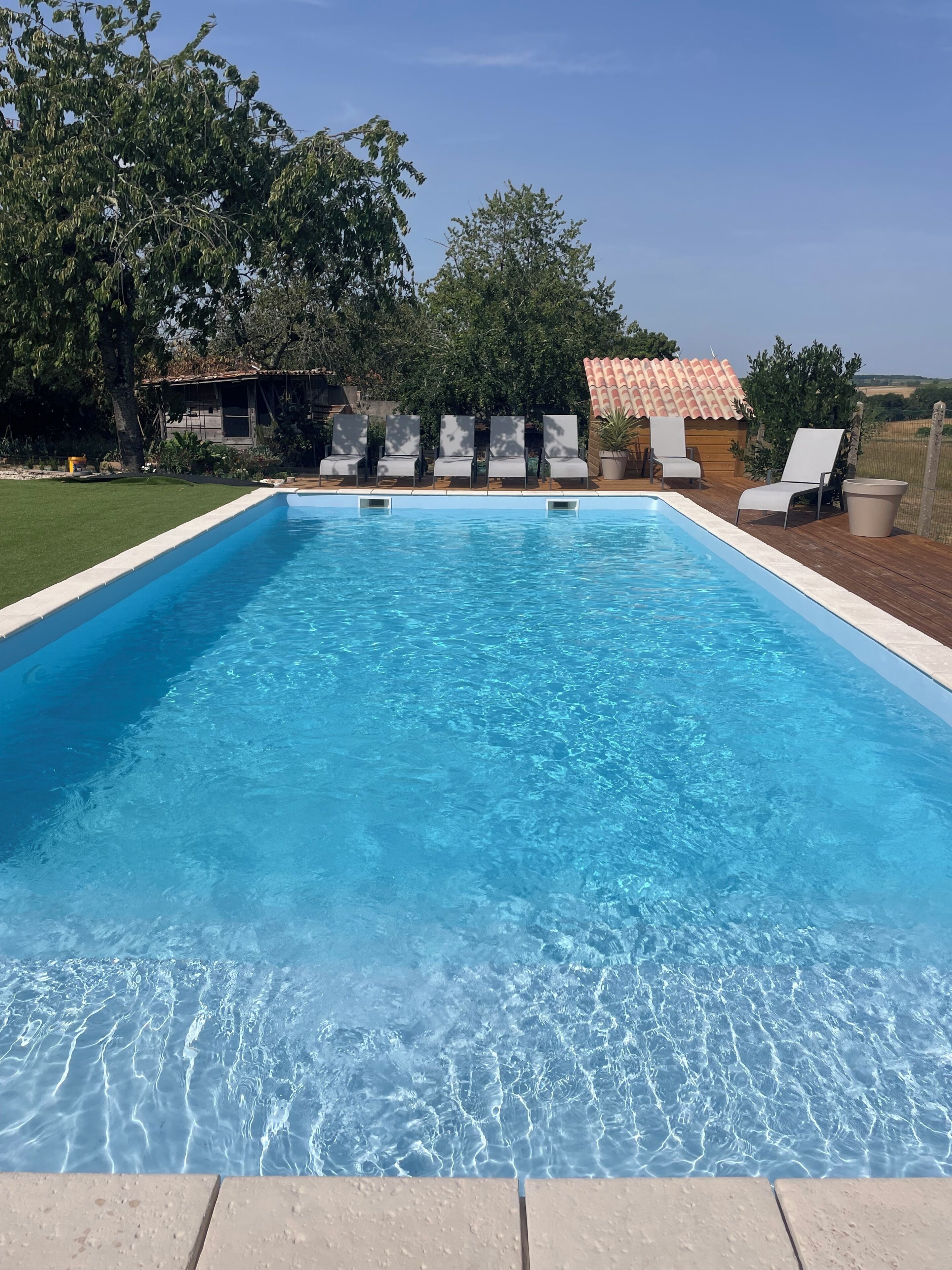 Une piscine rectangulaire à l’eau d’un bleu cristallin, entourée d’une terrasse en bois agrémentée de chaises longues.
