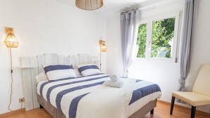 Ein Schlafzimmer mit einem Bett, zwei Nachttischlampen, einem Sessel und einem Fenster mit Vorhängen.