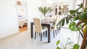 Ein moderner Essbereich mit großem Tisch und Stühlen, einer Topfpflanze und Blick ins Schlafzimmer.