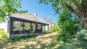 Ein modernes Haus mit großer Glasfront, einer überdachten Veranda und einem gepflegten Garten.