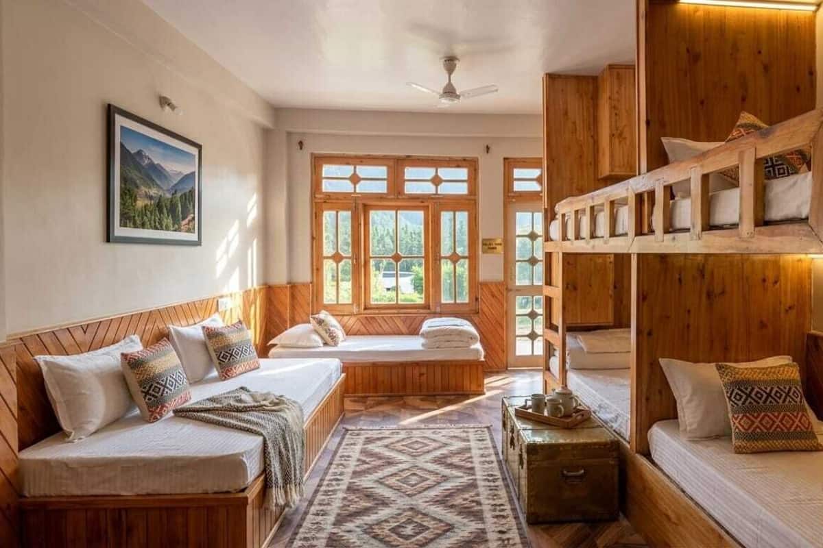 A room with a bunk bed, a sofa bed, and a window with a view of greenery.