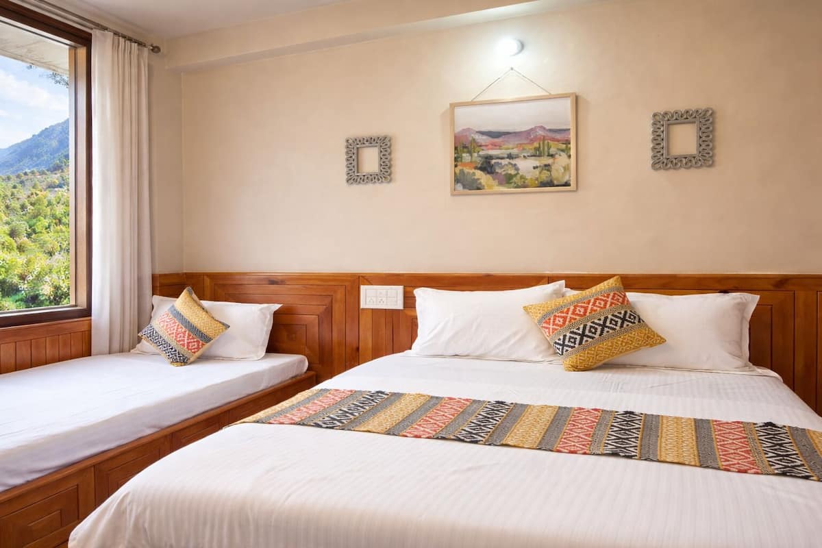 A hotel room with two beds, a view of greenery outside, and decorative wall art.