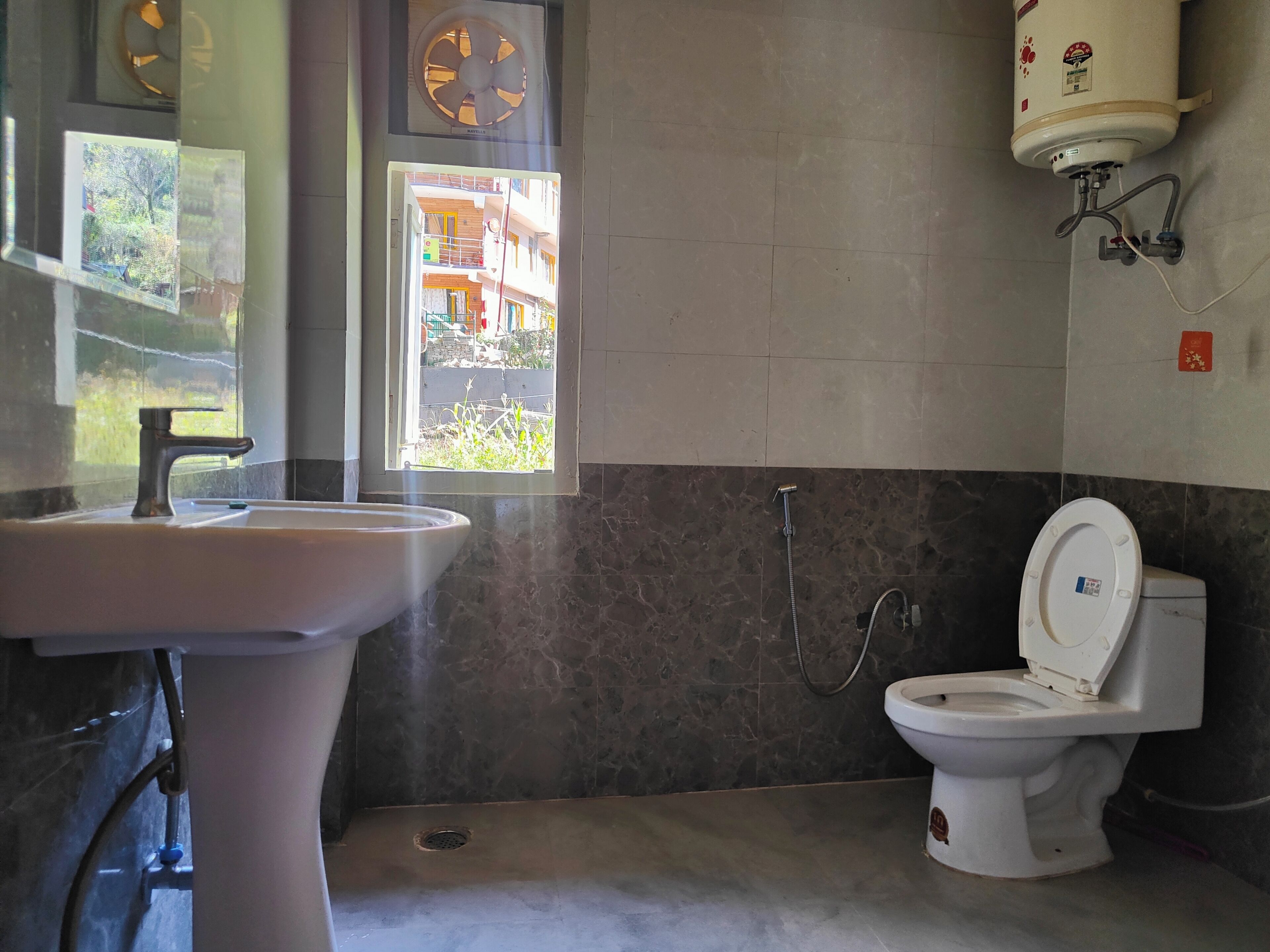 Ein Badezimmer mit Waschbecken, Toilette, Dusche und einem Fenster mit Blick auf ein Gebäude.