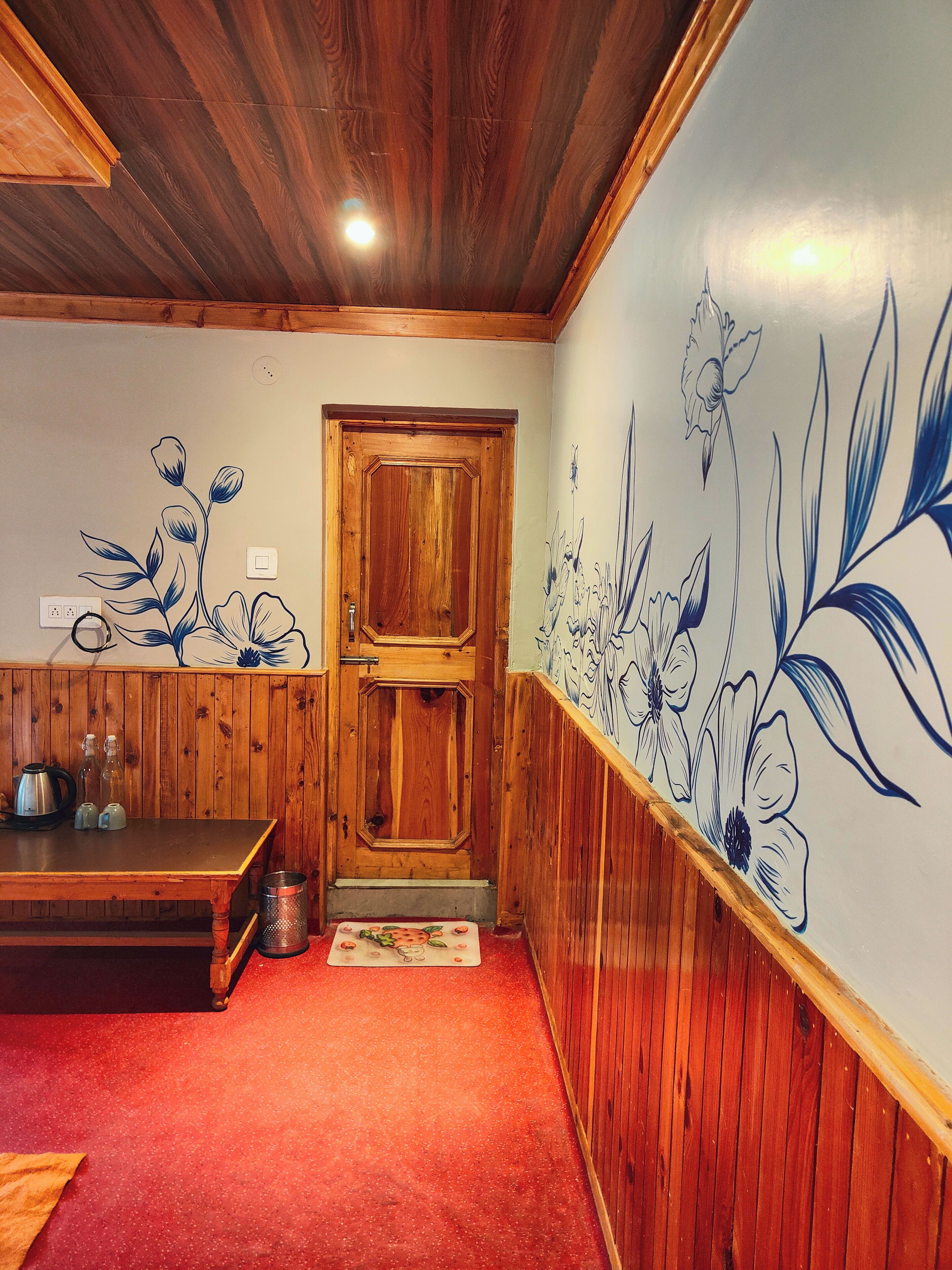 A wooden interior with a wooden door, a bench, and a wall with floral patterns.