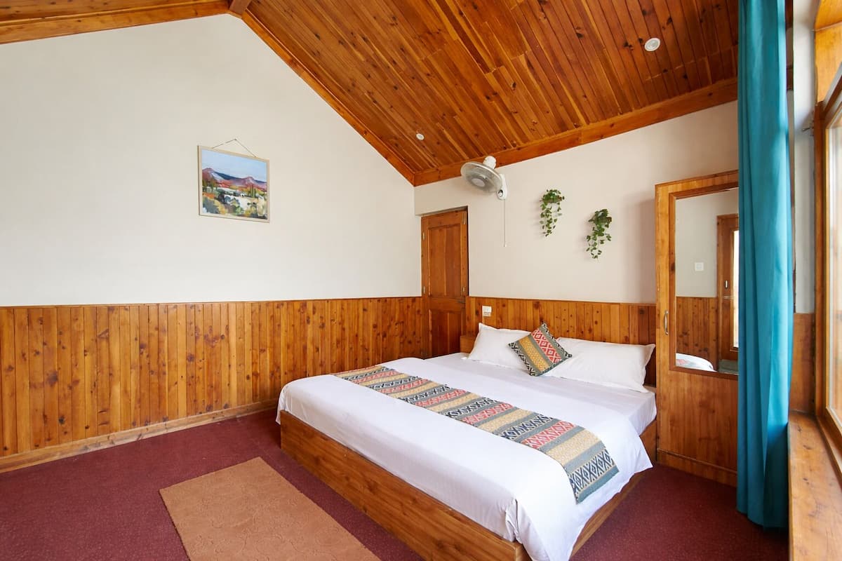 A wooden-paneled bedroom with a bed, a ceiling fan, a painting, and a mirror.