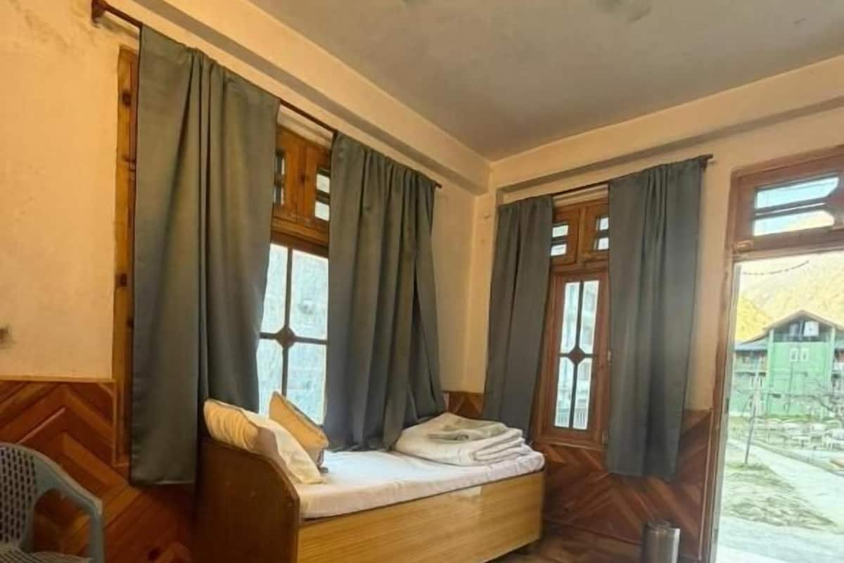 A room with a wooden bed, two windows with curtains, a chair, and a ceiling fan.