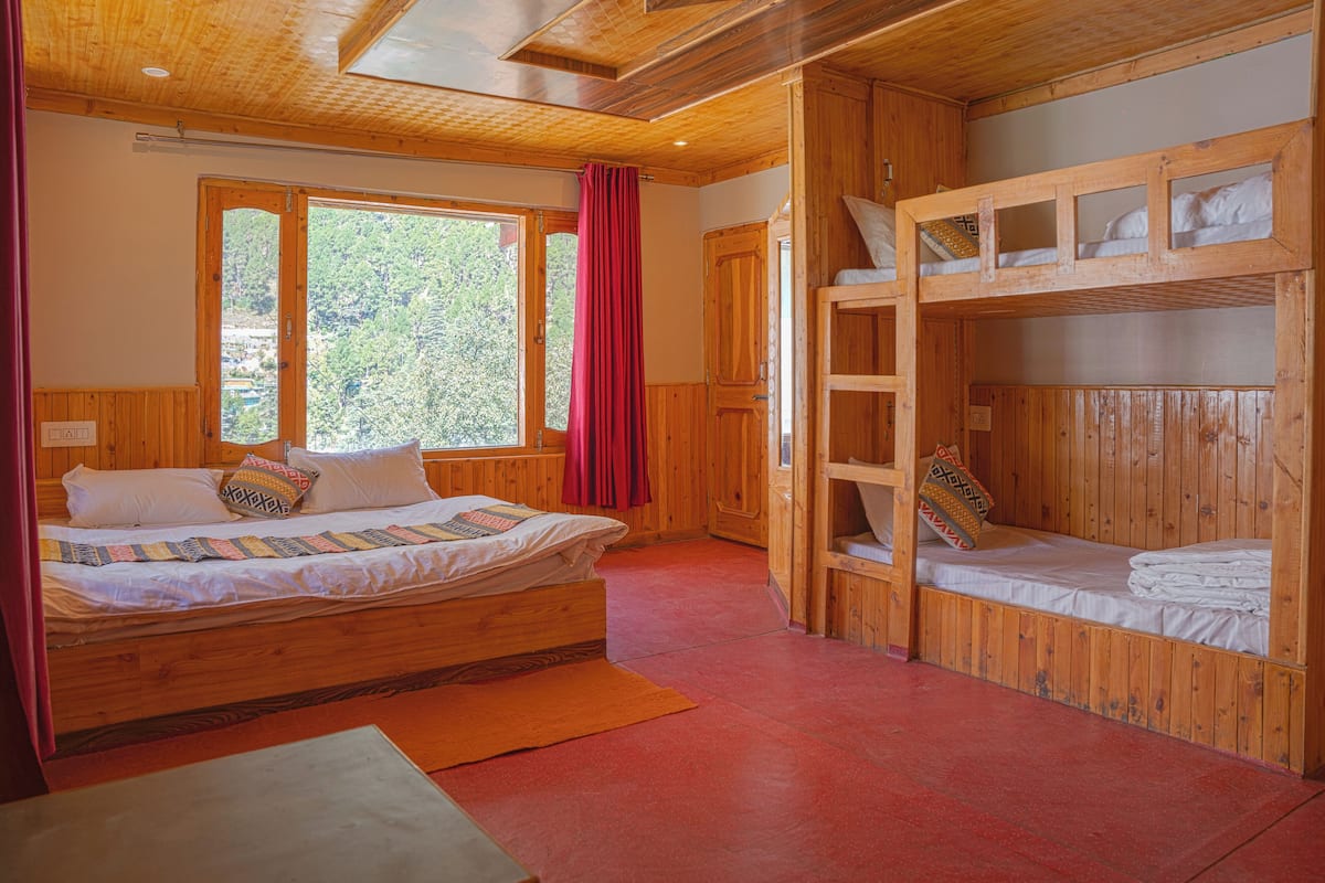 A wooden cabin bedroom with a single bed, a bunk bed, and a window with curtains.