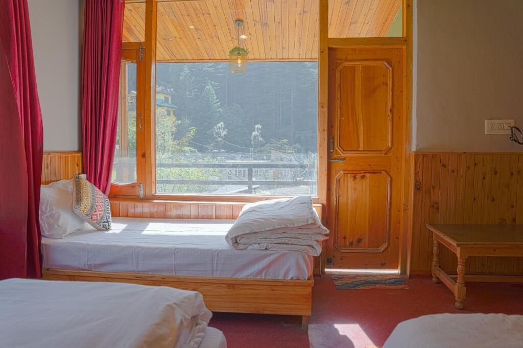 Una habitación con dos camas de madera, una puerta de madera y una ventana con vistas a árboles y un edificio.