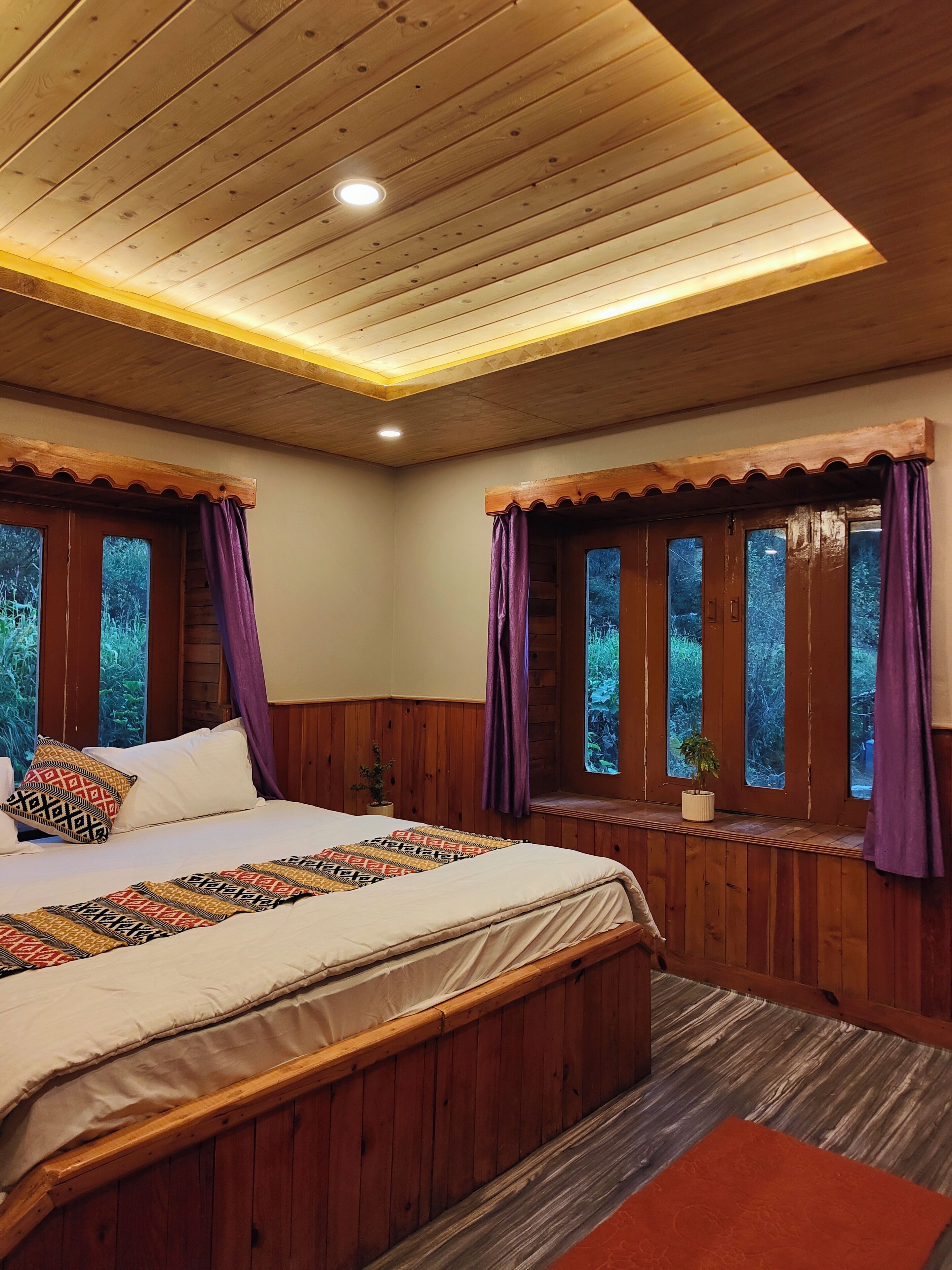 Un dormitorio con techo de madera, una cama con ropa de cama estampada y ventanas con cortinas.