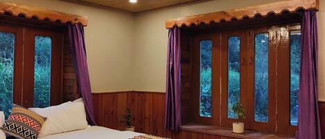 Un dormitorio con techo de madera, una cama con ropa de cama estampada y ventanas con cortinas.