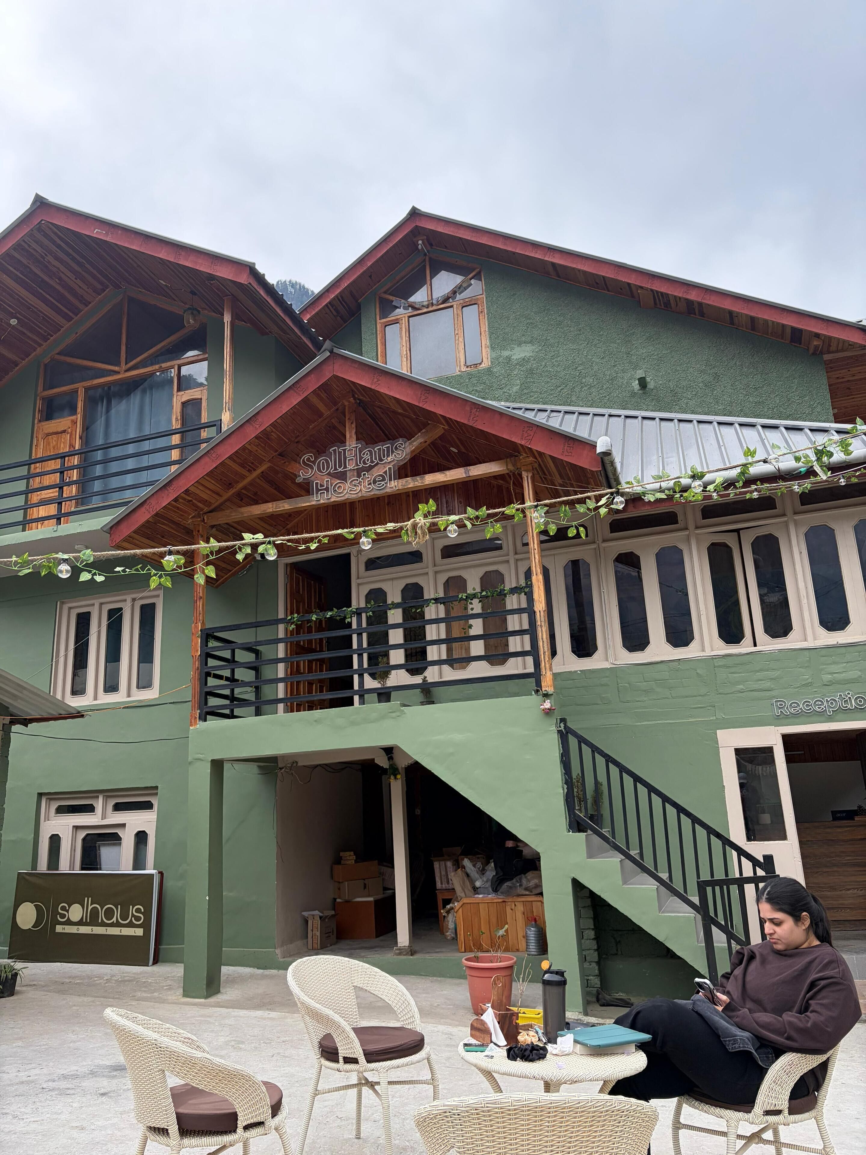 A hostel with a green exterior, wooden balconies, and wicker furniture.