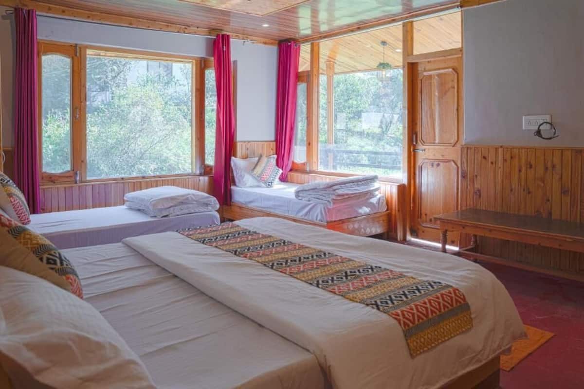 A room with two beds, wooden walls, large windows with curtains, and a bench.