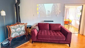 Ein Wohnzimmer mit einem roten Sofa, einem Vintage-Sessel, einem kleinen Tisch und einem großen Fenster mit Blick auf die Stadt.