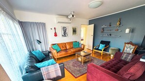 Ein Wohnzimmer mit Ledersofa, einem roten Samtsofa, einem Couchtisch aus Holz und einem gemusterten Teppich.