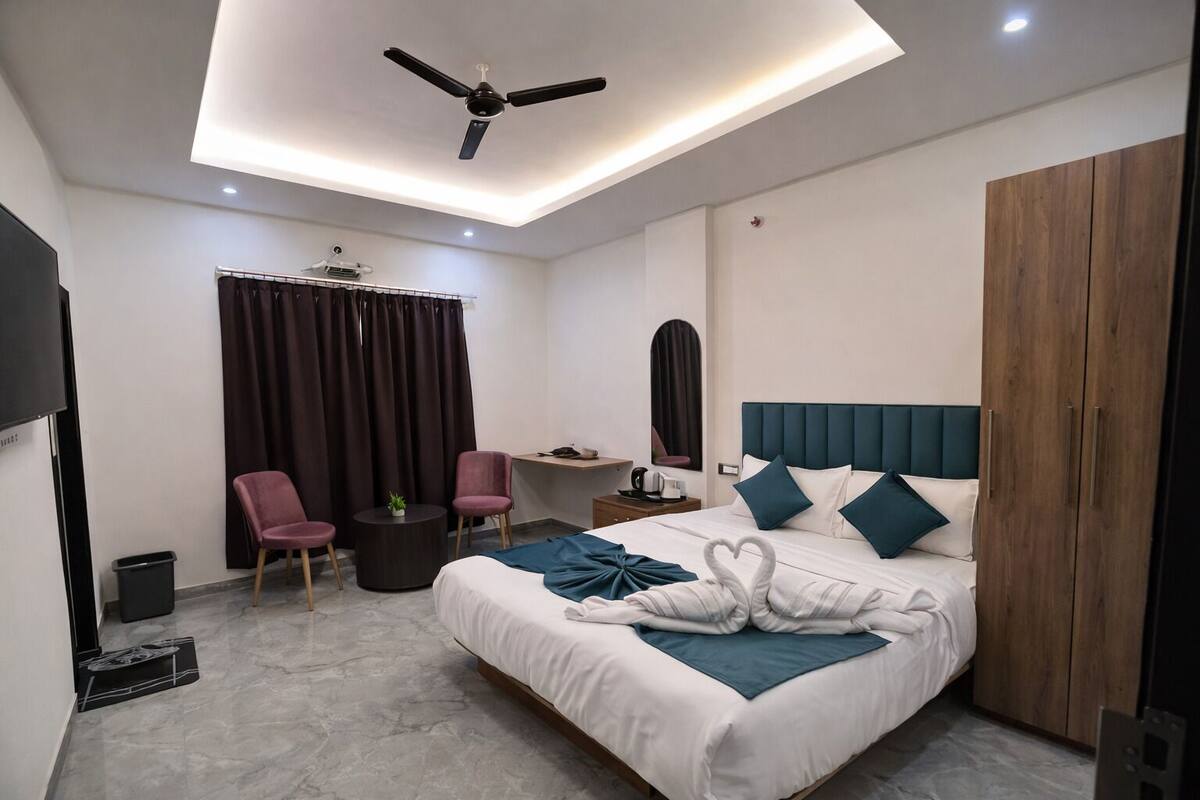 Ein modernes Hotelzimmer mit Bett, Schreibtisch, zwei Stühlen, Deckenventilator und Kleiderschrank.