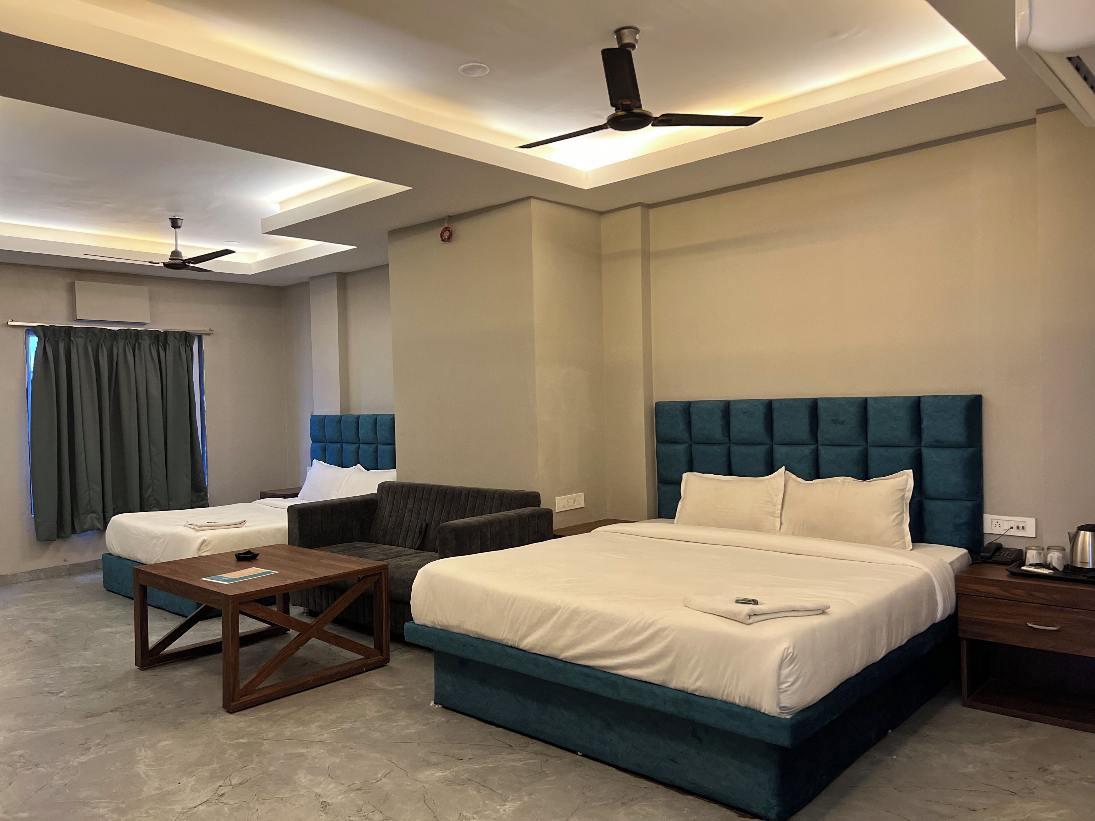 A hotel room with a large bed, two armchairs, a small table, ceiling fans, and recessed lighting.