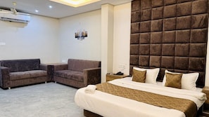 A hotel room with a bed, two sofas, a wall-mounted air conditioner, and a decorative wall panel. - Revelon Grand Hotel (Indore)