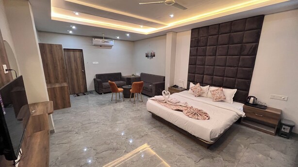 A modern hotel room with a large bed, a sofa, two armchairs, a ceiling fan, and a marble floor. - Revelon Grand Hotel (Indore)