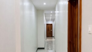 A long, narrow hallway with white walls and a polished marble floor. - Revelon Grand Hotel (Indore)
