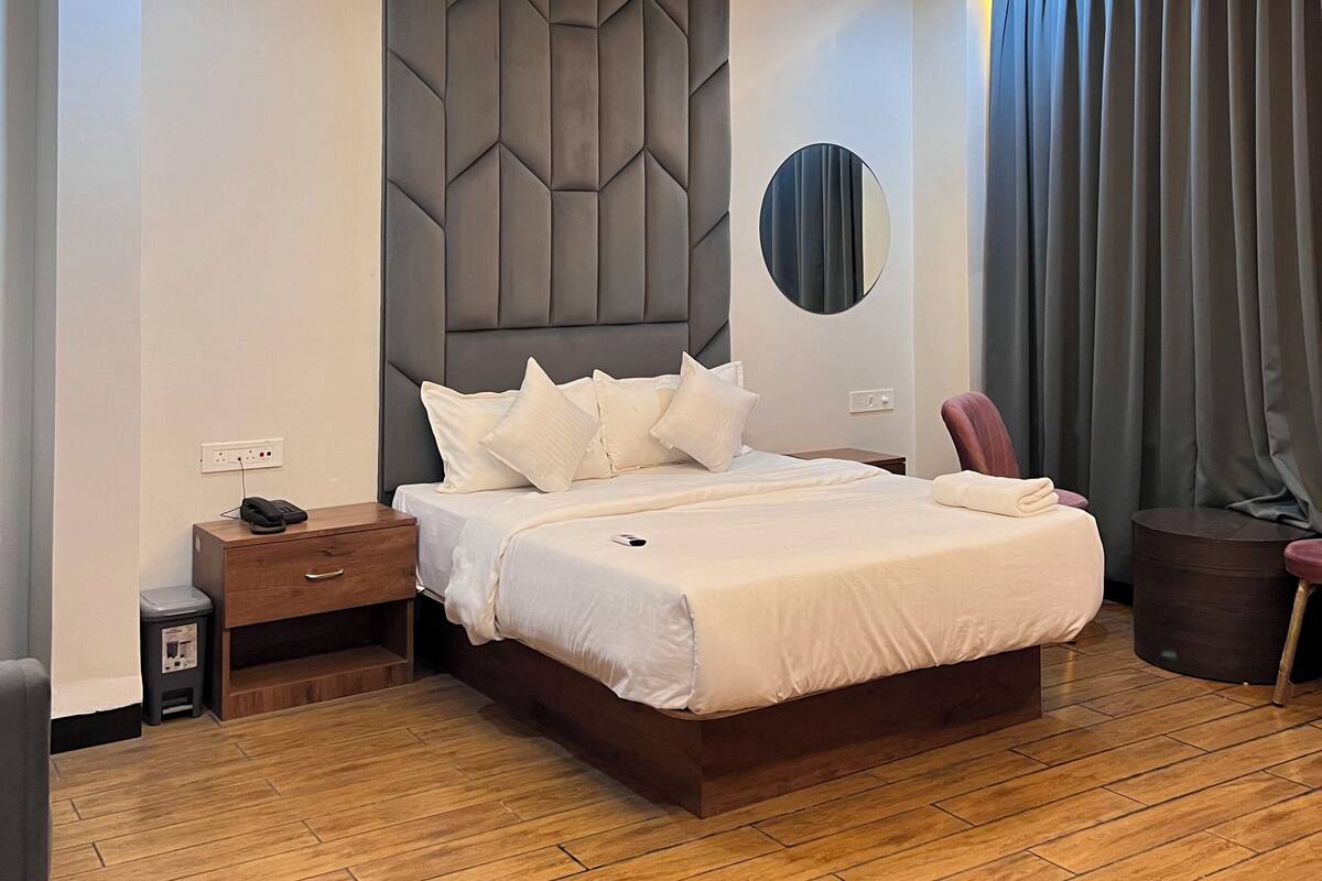 Ein modernes Hotelzimmer mit einem großen Bett, einem Deckenventilator, einem Nachttisch und einem kleinen runden Spiegel.