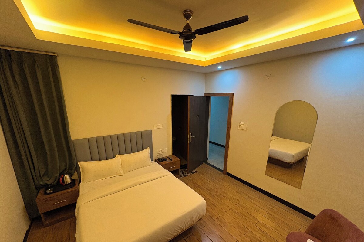 A hotel room with a bed, bedside table, nightstand, chair, ceiling fan, and a mirror on the wall.