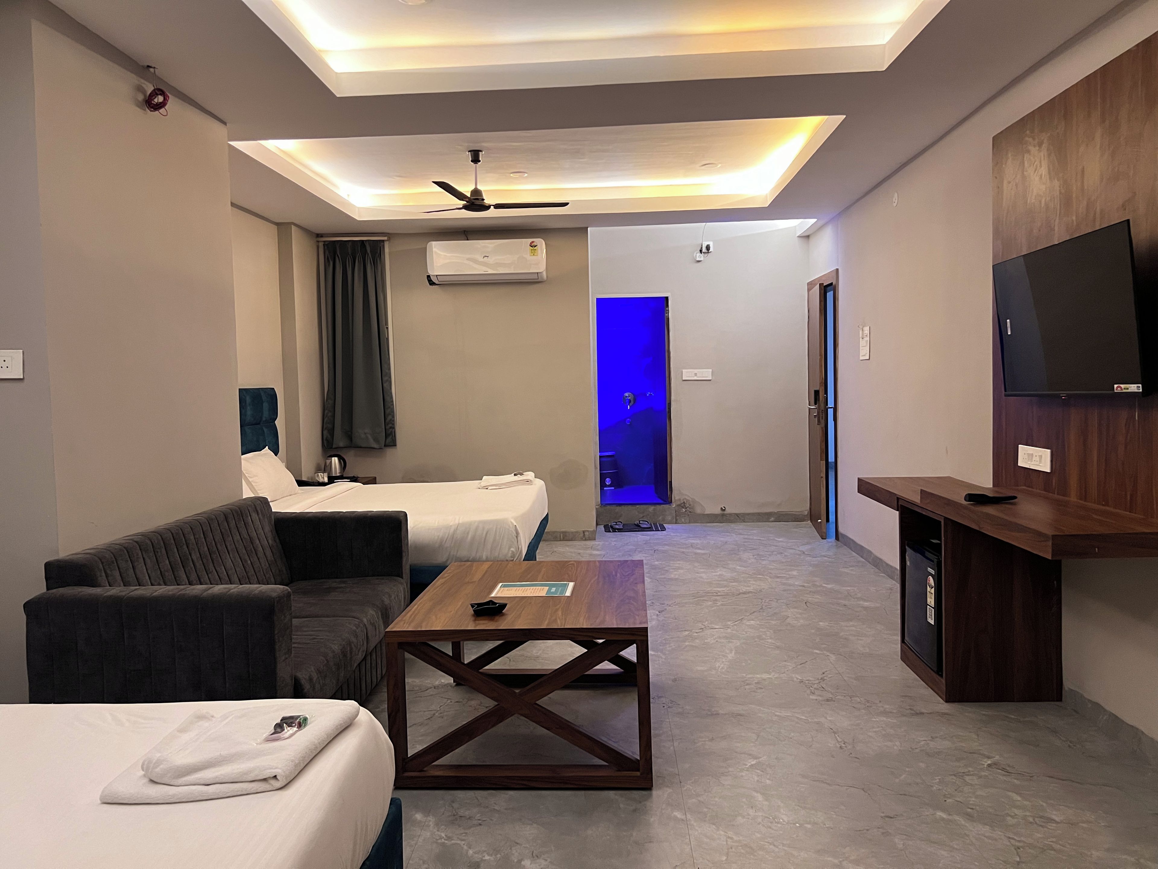 A hotel room with a bed, a sofa, a coffee table, a TV, and a ceiling fan.