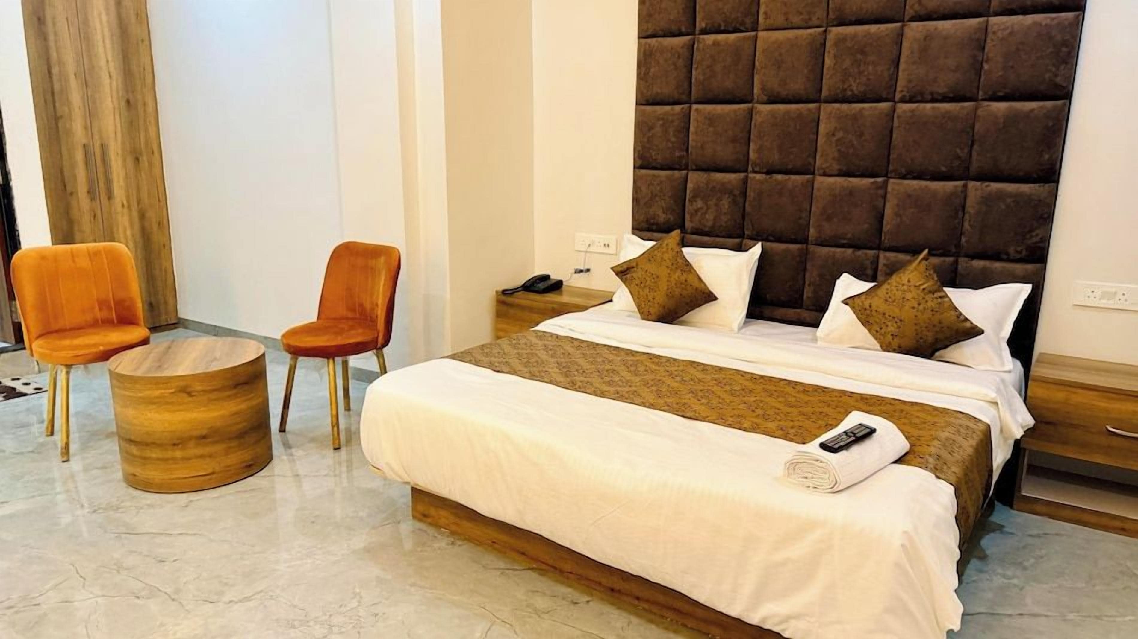 A hotel room with a bed, two chairs, a bedside table, and a wooden side table.