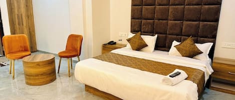 A hotel room with a bed, two chairs, a bedside table, and a wooden side table.