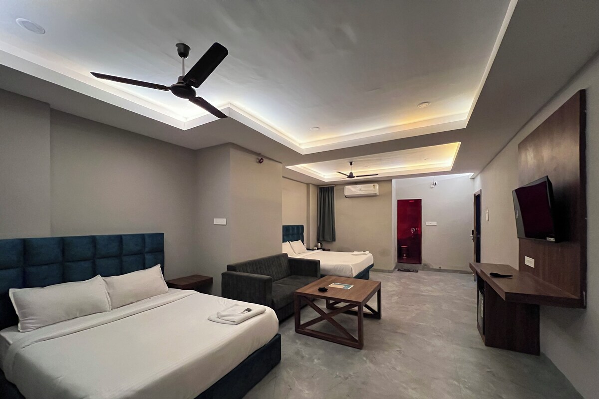 A hotel room with a bed, a sofa, a coffee table, a TV, and a ceiling fan.