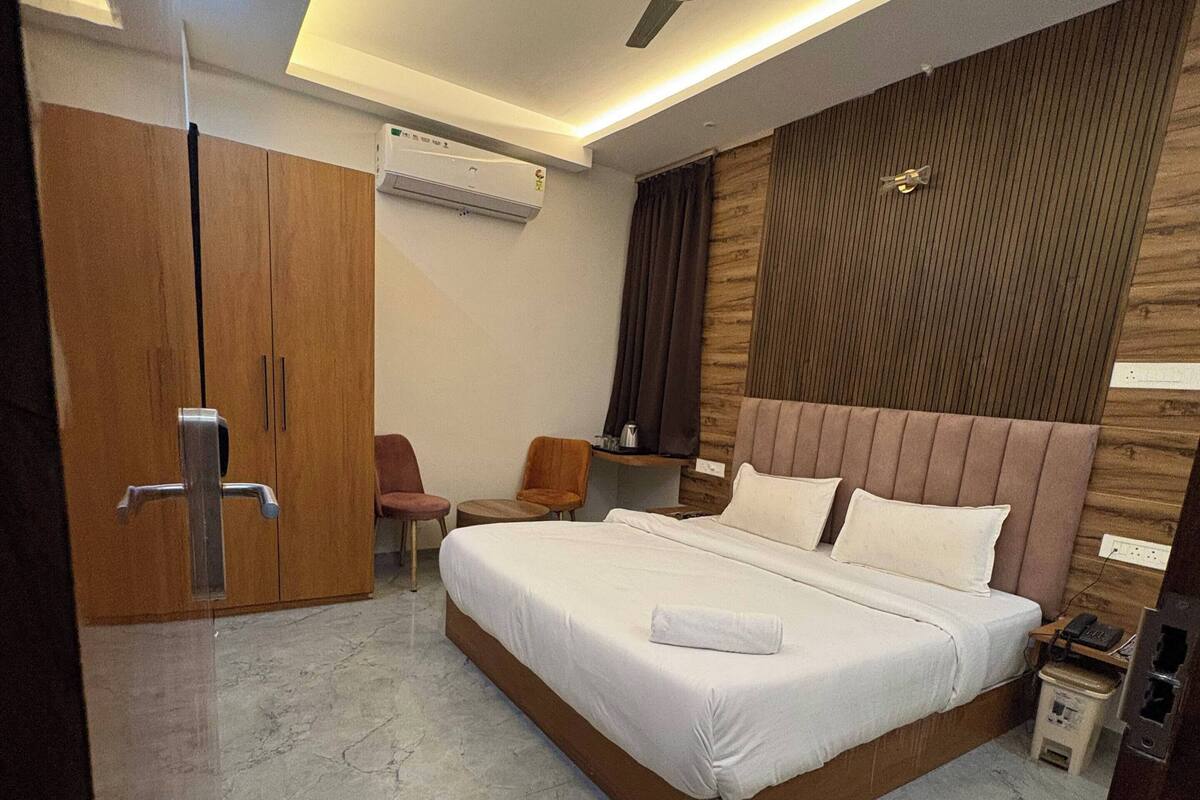 Ein modernes Schlafzimmer mit einem großen Bett, einem Deckenventilator, einem Holzschrank, einem kleinen Tisch mit Stühlen und einer wandmontierten Klimaanlage.