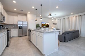 A modern kitchen with a central island, built-in appliances, pendant lighting, and a grey sofa in the adjacent living area. - Exclusive Villa, Full Resort Access! (Davenport)