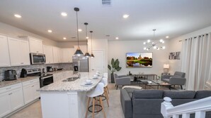 Una cocina moderna con armarios blancos, encimera de granito y una isla central con taburetes de bar.