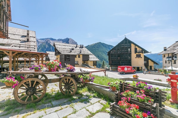 A wooden cart with flowers, a red delivery van, and buildings with mountain views. - La Piazzetta (Sauze di Cesana)