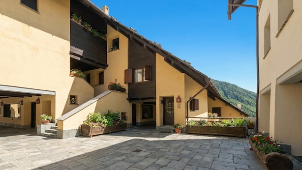 Ein Innenhof mit Steinpflasterung, einer Treppe und Gebäuden mit Balkonen und Blumenkästen.